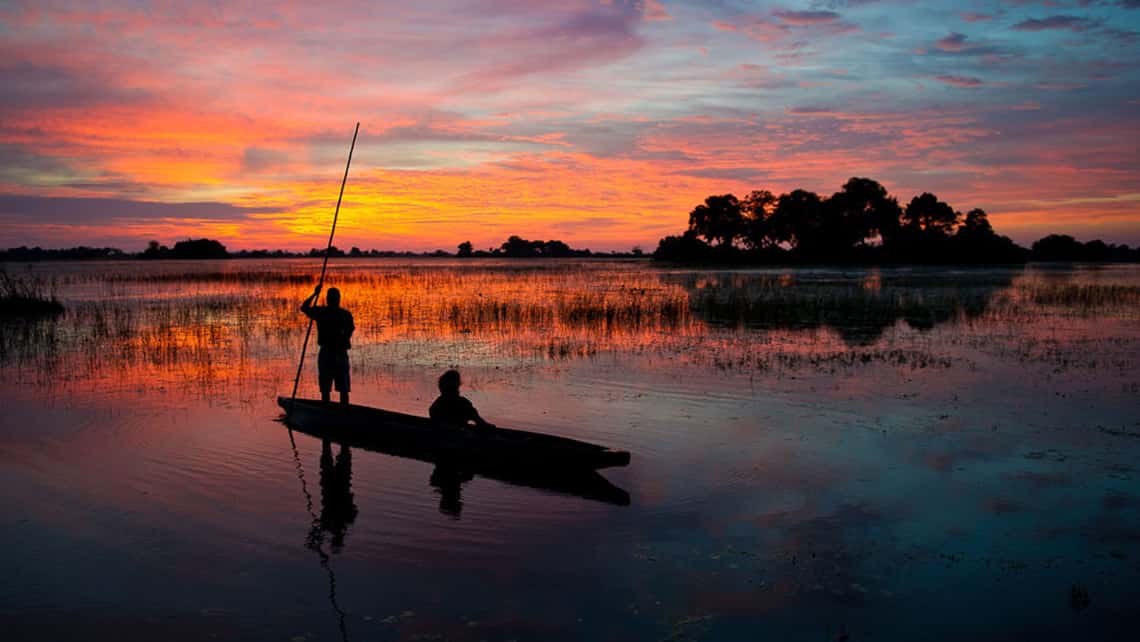 Mokoro mit Poler in der Abenddämmerung in der Lagune vor den Jao Camp